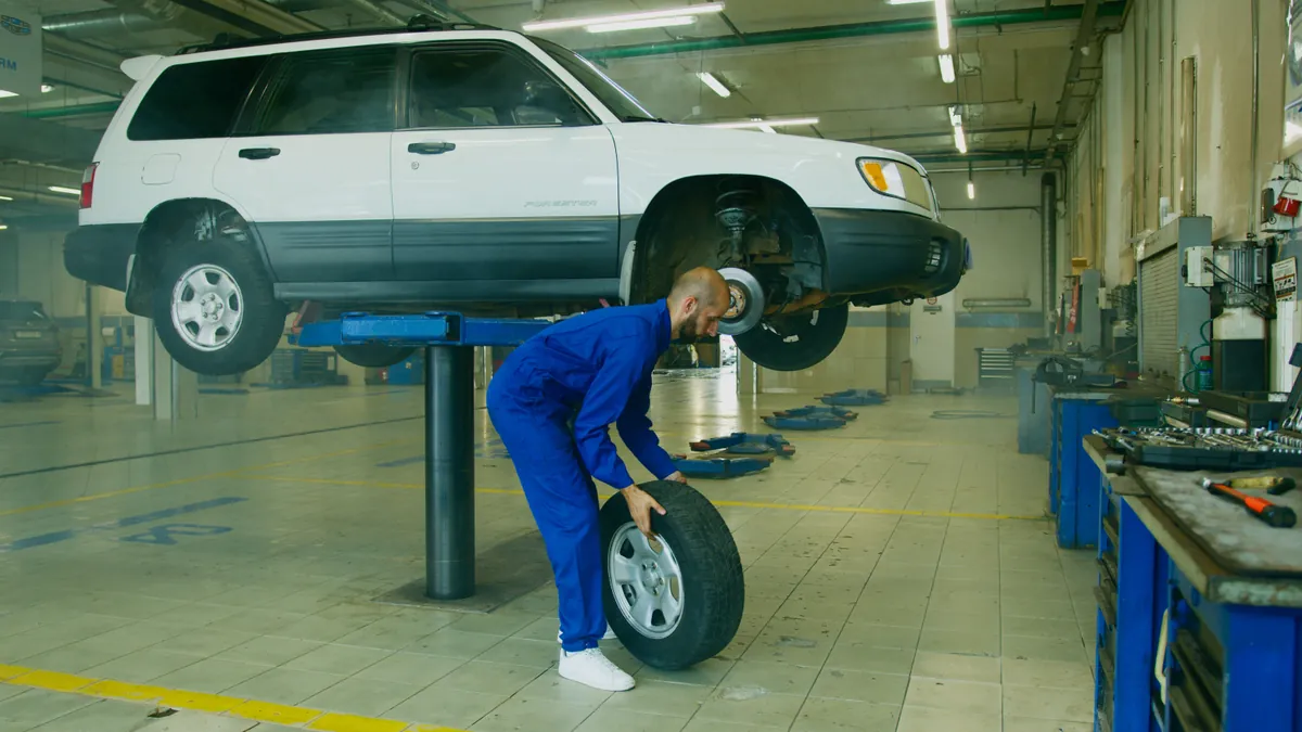 Mechanic handling a wheel beside a lifted car in an auto repair shop